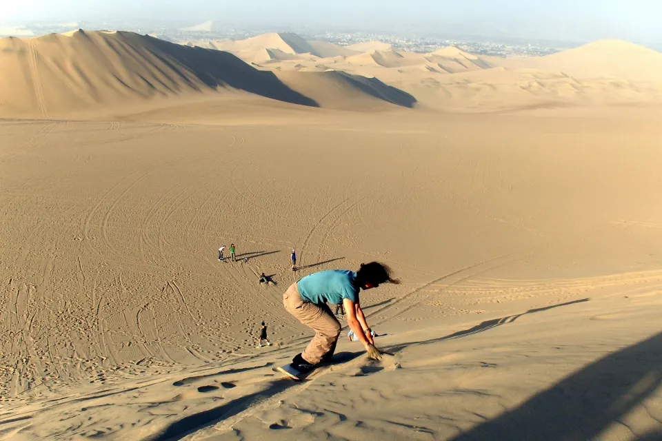 A young man sandboards standing up down a dune in the Ica desert