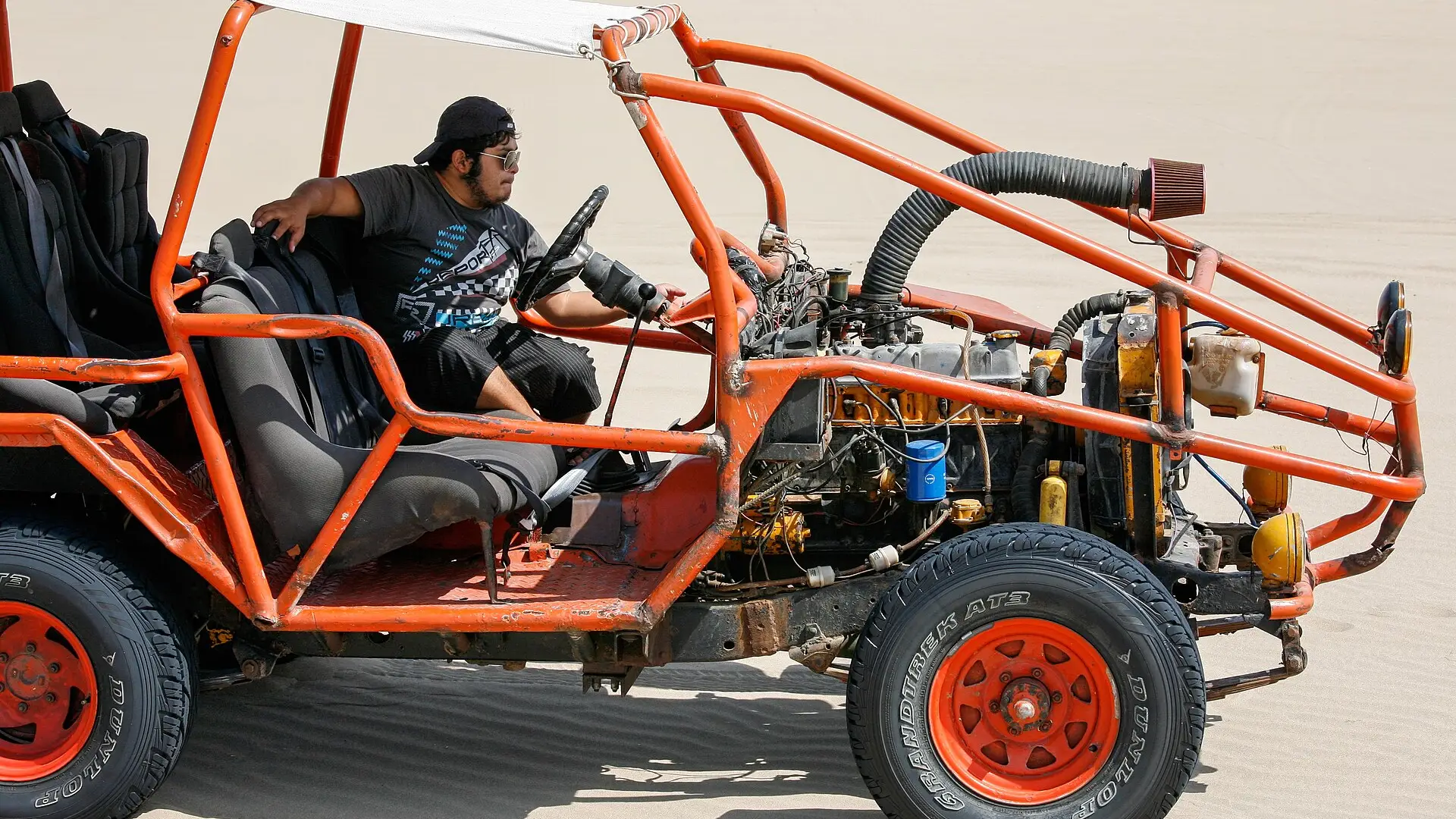 Un tubular naranja con su conductor sobre la arena de las dunas de Huacachina