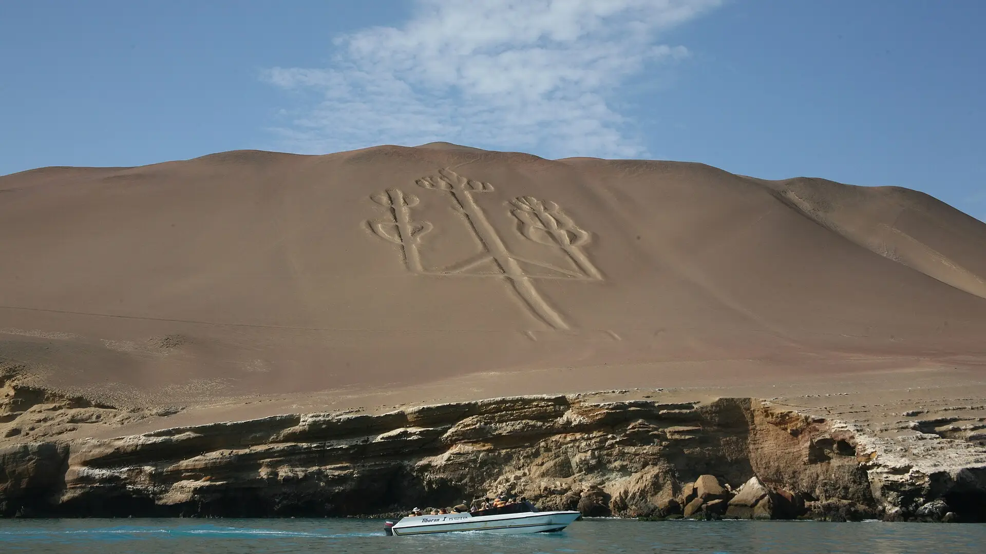 El Candelabro de Paracas dibujado en la ladera, con una lancha en el mar al pie